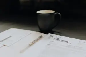 A pen, tax documents, and an envelope are on a desk next to a ceramic mug.
