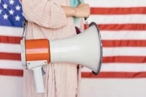 Person holding a megaphone in front of a blurred American flag backdrop.