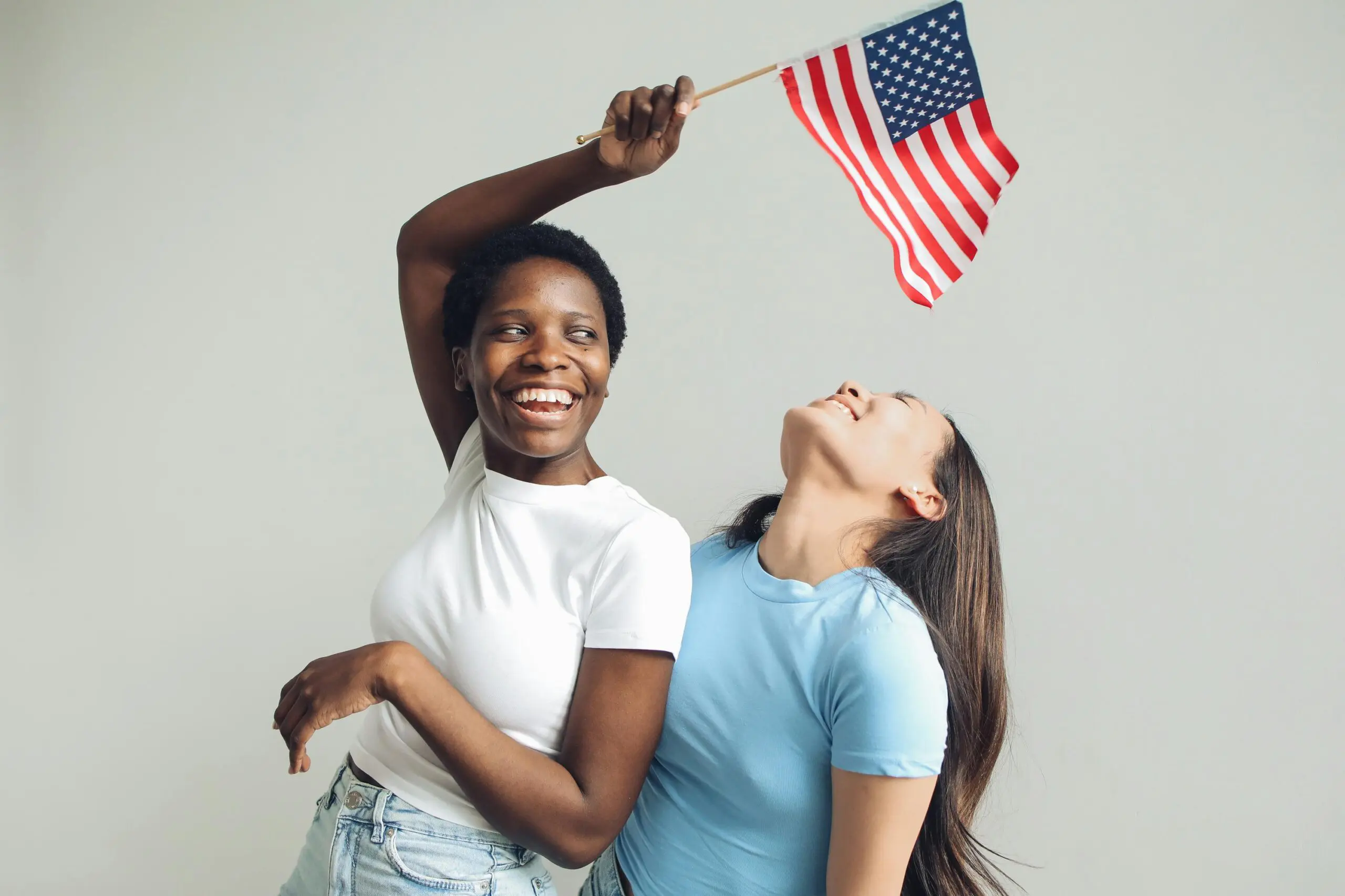 Dos mujeres sostienen una bandera estadounidense mientras exploran opciones de tarjeta de residencia para beneficiarios de DACA en Texas