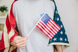 A person wearing a gray shirt holds a small American flag and is draped in a larger American flag.