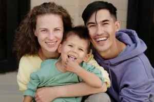 Three people, two adults and a child, are sitting together outdoors, smiling at the camera.