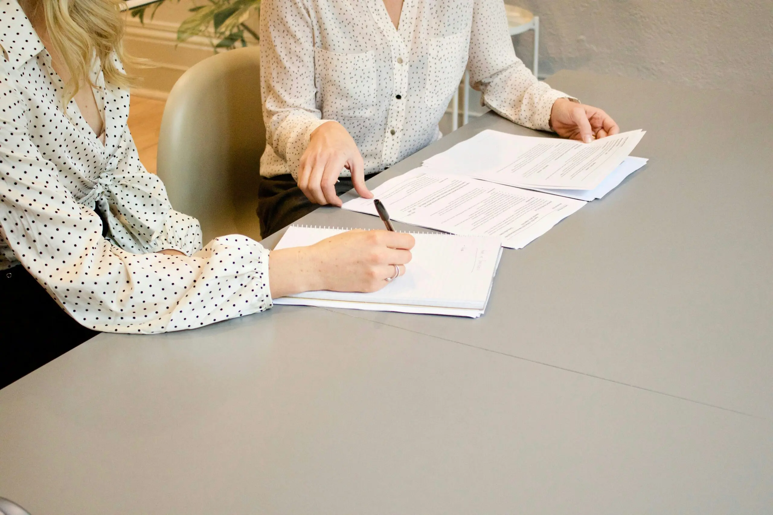 Two people in polka dot shirts sit at a table, reviewing and writing on documents spread out in front of them.