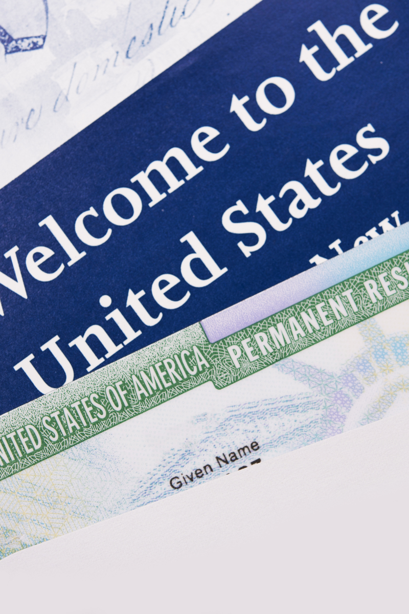 A close-up of a U.S. permanent resident card partially overlapping a "Welcome to the United States" document.