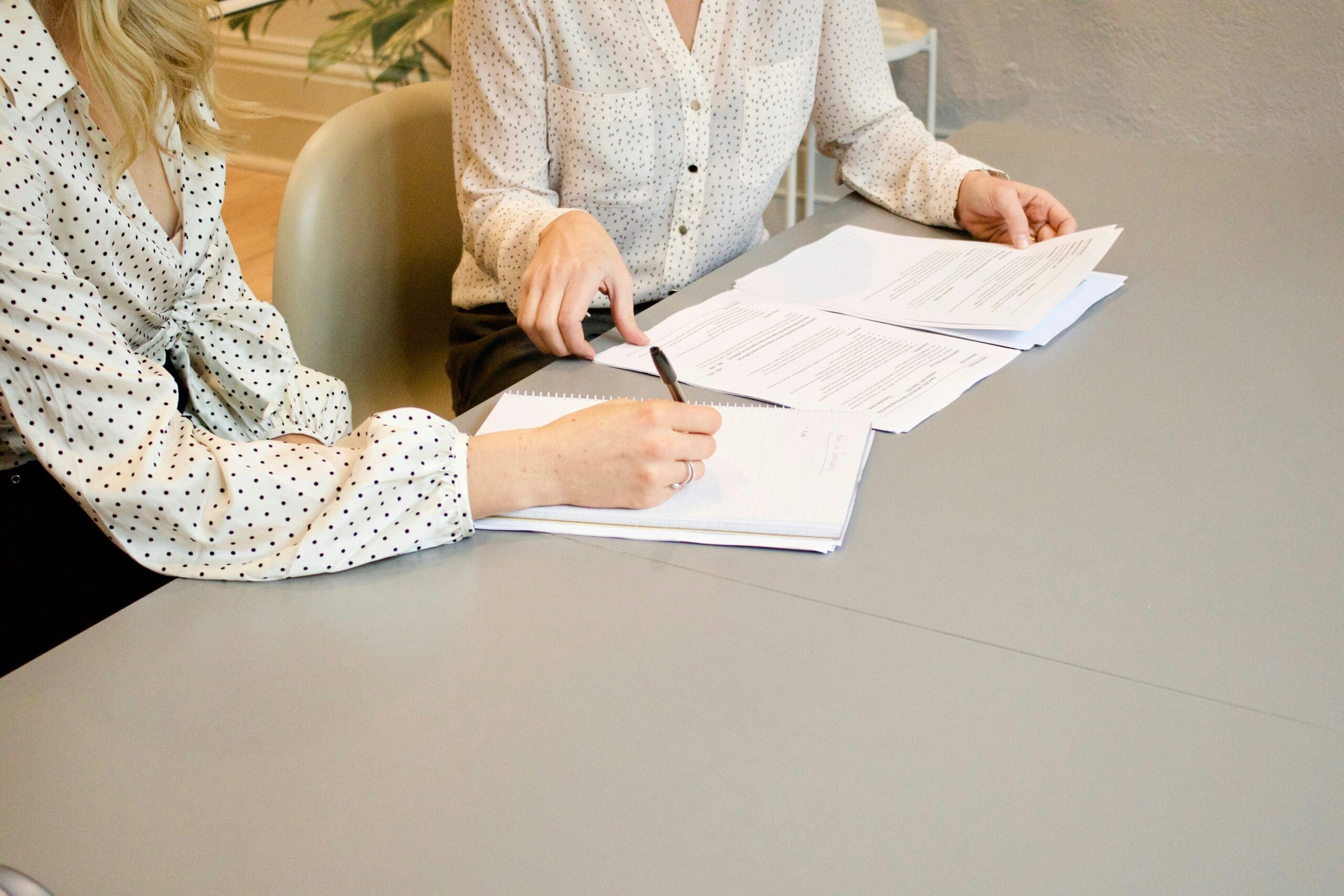 Two people in polka dot shirts sit at a table, reviewing and writing on documents spread out in front of them.