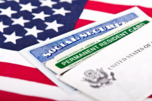 A Social Security card and green Permanent Resident Card rest on an American flag, representing the shift from conditional to permanent residency under Form I-751.