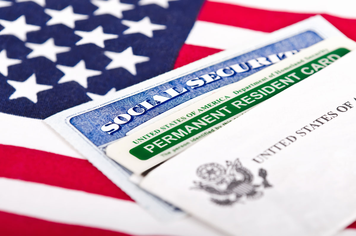 A Social Security card and green Permanent Resident Card rest on an American flag, representing the shift from conditional to permanent residency under Form I-751.