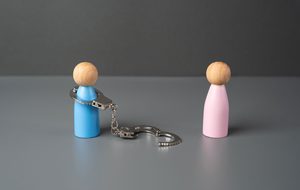 Two small figures stand apart, one wearing an open, unlocked handcuff connected by a chain, symbolizing freedom from a controlling relationship.