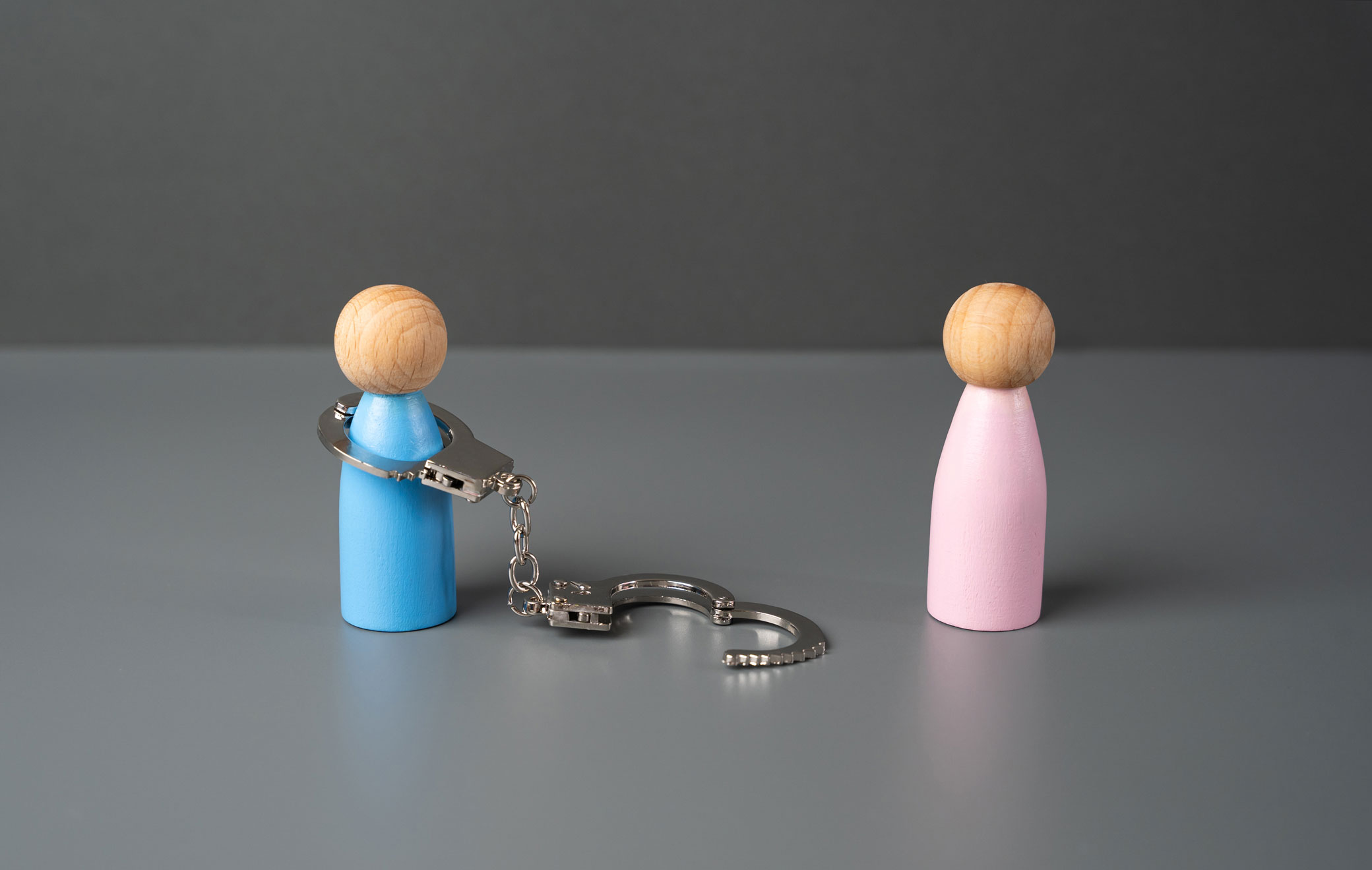 Two small figures stand apart, one wearing an open, unlocked handcuff connected by a chain, symbolizing freedom from a controlling relationship.